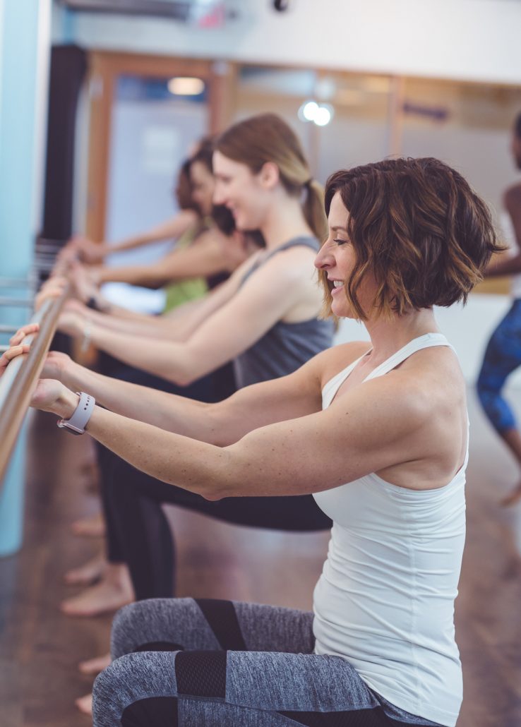 Multiethnic group of women do a barre workout together in a modern health club